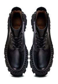Paire de bottines noires en cuir à lacets avec semelles épaisses rainurées et fermetures éclair latérales, vues de dessus sur fond blanc.