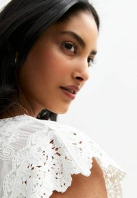 Witte kanten blouse met intricatere patronen op de mouwen, van zachte, vloeiende stof en met een ontspannen pasvorm, die de halslijn accentueert.