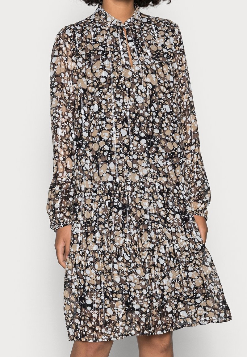 Lång, utsvängd klänning med hög krage. Gjord av lättviktsmaterial med ett abstrakt mönster av bruna, vita och svarta cirklar. Långa ärmar, flera lager design.