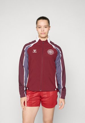Maroon sports jacket with striped sleeves in purple and white. Zippered front, logo on chest, paired with red shorts featuring a logo.