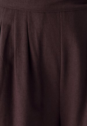 Mørkebrun stof med en tekstureret overflade, der har folder og en elastisk talje. Designet fremhæver en glat, flydende form.