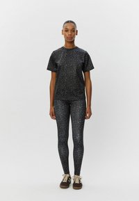 T-shirt a legíny v čiernej leopardovej potlači, vyrobené z elastického materiálu. Má okrúhly výstrih a krátke rukávy. Celkový vzhľad dopĺňajú pohodlné tenisky.