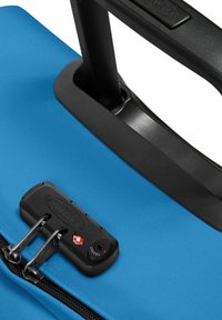 Borsa da viaggio blu con tessuto texturizzato, dotata di una chiusura a zip nera e un manico telescopico attaccato a una base in plastica liscia.