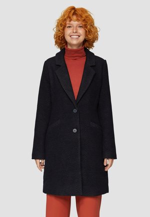 Zwarte visgraatjas met een notch kraag, twee knopen en zijzakken. Draagt over een rode coltrui, met een slim fit.