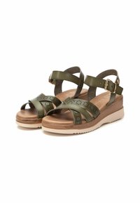 Sandalias verde oliva con dos correas cruzadas y una correa en el tobillo, con patrones florales recortados, sobre una suela de cuña de color beige claro.