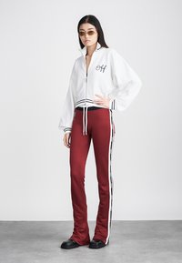 White zip-up jacket with "Off" logo, black stripes, and balloon sleeves paired with burgundy pants featuring side stripes and a tight fit. Black shoes.