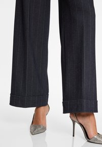 Wijdvallende pinstripe broek van donkerblauwe stof, met een omgeslagen zoom en gecombineerd met zilveren slingback hakken.