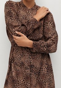 Robe marron à manches longues avec un motif léopard à taches noires, un col montant et des manches légèrement bouffantes.