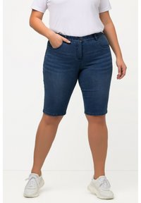 Shorts en jean bleu foncé avec une taille mi-haute, des poches avant et une coupe ajustée. Finition avec un ourlet propre et associés à des baskets blanches.