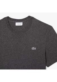 T-shirt grigia in cotone con scollatura rotonda, maniche corte e un piccolo logo ricamato del coccodrillo Lacoste sul petto sinistro. Vestibilità regolare.
