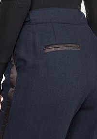 Fjortonblå skräddarsydda byxor med herringbone-mönster, satinaccent på sidorna och en bakficka med satinglansdetalj.