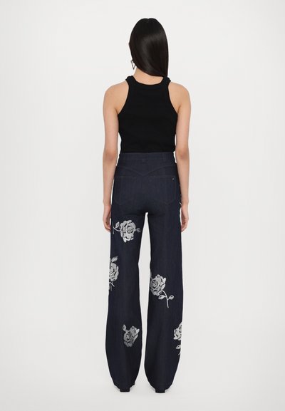 Donkerdenim wijde broek met zilveren bloemenborduurwerk op de heupen, gecombineerd met een zwarte aansluitende tanktop. Gladde stof met een getailleerd ontwerp.
