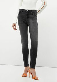 Slim-fit mustat farkut, joissa on valkoinen pitkähihainen paita ja kirkkaan oranssit avokkaat korkokengät.