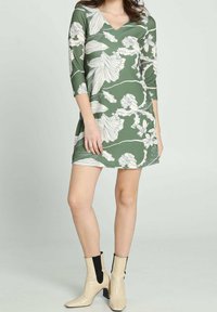 Zielona sukienka w kwiaty z dekoltem w serek i rękawami do łokcia, z fakturowanym wzorem. Połączona z beżowymi i czarnymi botkami za kostkę.