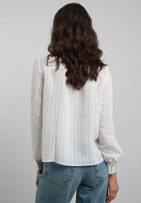 Camicia bianca a maniche lunghe con righe verticali testurizzate e polsini abbottonati, abbinata a jeans azzurri a vita alta.