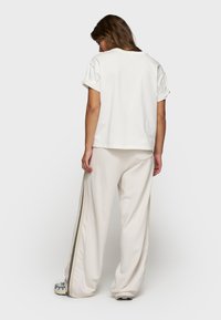 Witte katoenen t-shirt met opgerolde korte mouwen, gecombineerd met crèmekleurige, wijde broek met zwarte zijstrepen en een ontspannen pasvorm.