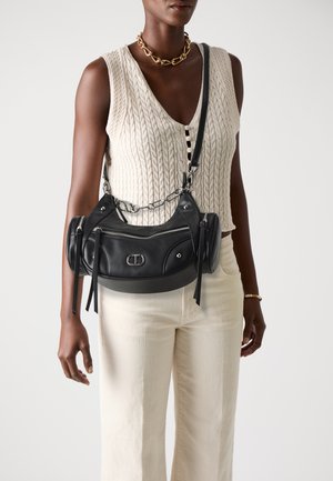 Black leather handbag with zippered pockets, silver hardware, and a chain strap. Features a curved shape and tassel accents.