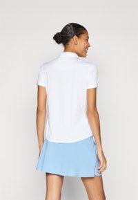 Chemise polo blanche à manches courtes et col, associée à une jupe-short bleu clair avec un ourlet évasé et des poches latérales.