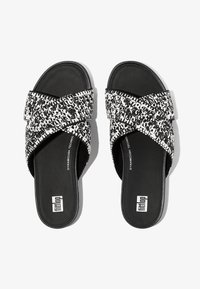 Zwart-witte slide sandalen met kruisen textiele banden, platte zolen en een gladde zwarte binnenkant; heeft 'fit flop' branding op de onderkant.