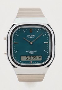 Casio kvarcinis laikrodis su stačiakampiu žaliu ciferblatu, nerūdijančio plieno korpusu ir sidabriniu metaliniu dirželiu. Su skaitmeniniu ekranu ir vandens apsaugos ženklu.