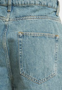 Jeans de mezclilla de un azul claro que muestran un primer plano del bolsillo trasero con detalles de costura visibles y una textura ligeramente desgastada.