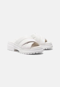 Witte slide sandalen hebben gekruiste banden van glad materiaal, een gevoerde inlegzool en een chunky, gestructureerde witte buitenzool.