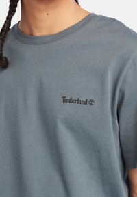 Šedé bavlněné tričko s kulatým výstřihem. Na levé straně hrudi je malé černé logo Timberland. Měkký materiál, krátké rukávy.