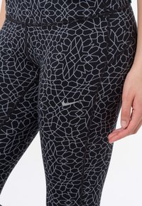 Leggings neri con un motivo geometrico grigio, realizzati in materiale elasticizzato. Inclusa una piccola etichetta Nike e cuciture piatte per il comfort.