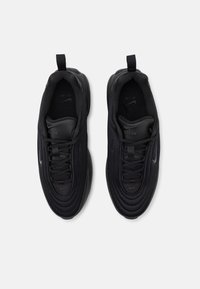 Baskets de sport noires avec une tige en mesh texturé, lacets ronds et bout renforcé. Présente un logo "Air" bien visible et une languette au niveau du talon.
