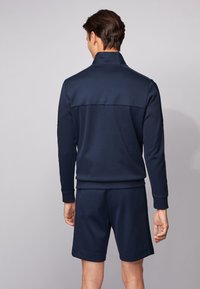 Chándal deportivo color azul marino con cuello alto y puños acanalados, que presenta un diseño sólido y un corte relajado. Los pantalones cortos complementan la parte superior.