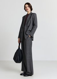 Costume gris sur mesure avec un blazer croisé et un pantalon à jambes larges, associé à un haut en maille bordeaux et un sac à main en cuir noir.