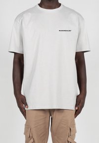 Kortærmet lysegrå t-shirt lavet af bomuld, med et lille sort logo tekst på venstre brystområde. Enkel, afslappet pasform.