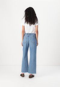 Jeans de mezclilla azul claro de pierna ancha con dobladillos deshilachados, que presentan una cintura alta y bolsillos traseros, combinados con una camiseta blanca y unas bailarinas estampadas.