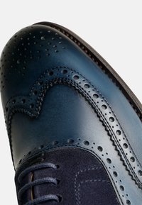 Scarpa da uomo in pelle blu navy, modello wingtip, con dettagli perforati, superficie liscia, pannello in suede a contrasto e chiusura con lacci tradizionale.