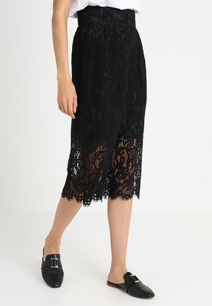 Black lace skirt with a high waist, featuring floral patterns and a scalloped hem. Paired with black slip-on shoes.