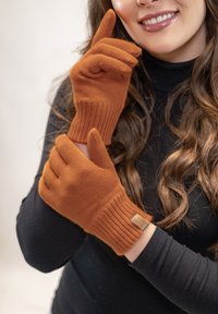 Guanti arancioni lavorati a maglia con polsini a costine, dotati di un piccolo etichetta del marchio. Il materiale sembra morbido e dal tatto texturato, in armonia con un top nero.