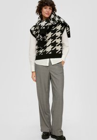 Čierny a biely houndstooth pletený sveter preložený cez bielu košeľu, v kombinácii s širokými čiernymi a bielymi károvanými nohavicami a platformovými topánkami.