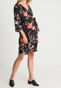 Schwarzes Wickelkleid mit Dreiviertelärmeln, das ein Blumenmuster in rosa und orange Tönen aufweist und einen Bindegürtel in der Taille hat.