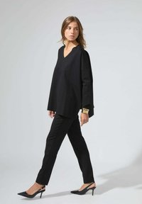 Tunique noire oversize avec un col en V, associée à un pantalon noir ajusté et des talons noirs. Texture lisse, design minimaliste, accents élégants.