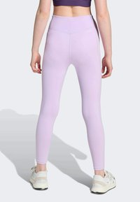 Lila leggings med hög midja, elastiskt material, jämn textur och detaljer med kontrastsömmar, som är kombinerade med vita sportskor.
