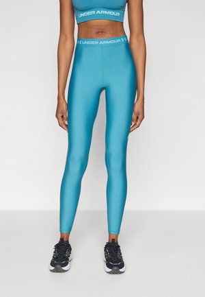 Leggings deportivos turquesa con textura suave y cintura alta que lleva el logotipo de Under Armour. Combinados con zapatillas deportivas negras.