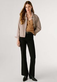 Chaqueta a rayas en beige y marrón, blusa marrón y pantalones acampanados negros. Cinturón negro con hebilla redonda, combinado con botines de tacón.