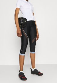 Pantaloni da ciclismo neri con pannelli in mesh, accenti blu chiaro e vestibilità aderente. Abbinati a una maglietta bianca a maniche corte e un casco nero.
