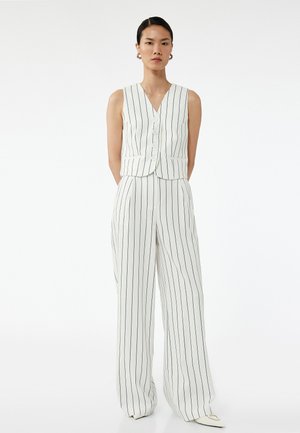 Biały top bez rękawów w pasy z dekoltem w kształcie litery V, pięcioma guzikami i dopasowanymi spodniami w szerokiej nogawce. Materiał jest gładki z granatowymi paskami.