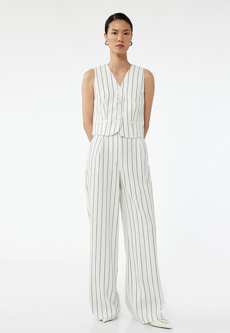 Biały top bez rękawów w pasy z dekoltem w kształcie litery V, pięcioma guzikami i dopasowanymi spodniami w szerokiej nogawce. Materiał jest gładki z granatowymi paskami.