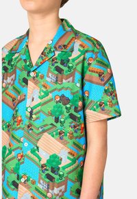 Camisa de manga corta con un gráfico colorido inspirado en Minecraft que presenta personajes pixelados, fondo verde y cierre de botones.