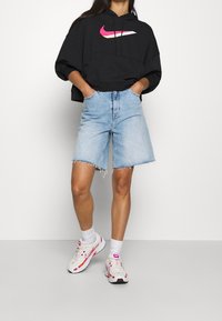 Černá krátká mikina s růžovým logem Nike, světle modré džínové kraťasy s třepeným lemem a bílé tenisky s růžovými akcenty.