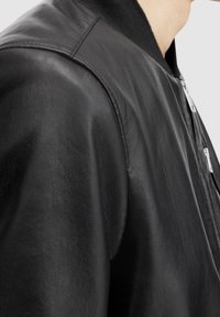 Svart läderbomberjacka med en strukturerad yta, som har dragkedja och ribbad krage. Väger in axeldetaljer och har en overall elegant design.