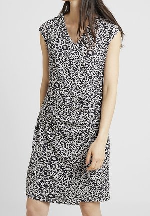 Mujer con vestido sin mangas hasta la rodilla de estampado de leopardo en blanco y negro, con escote en V y detalle fruncido en la cintura.