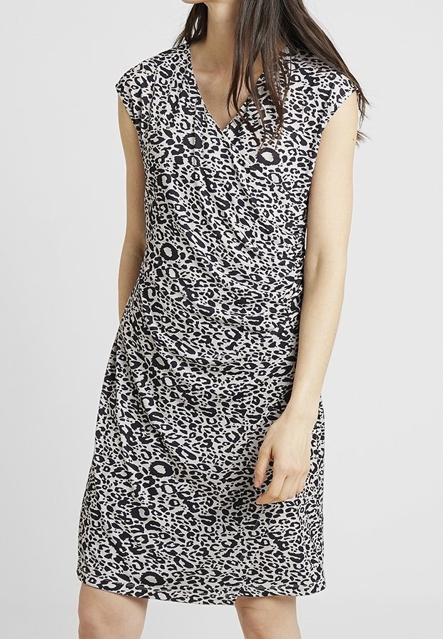 Femme portant une robe sans manches, imprimé léopard noir et blanc, longueur genoux, avec col en V et taille froncée.